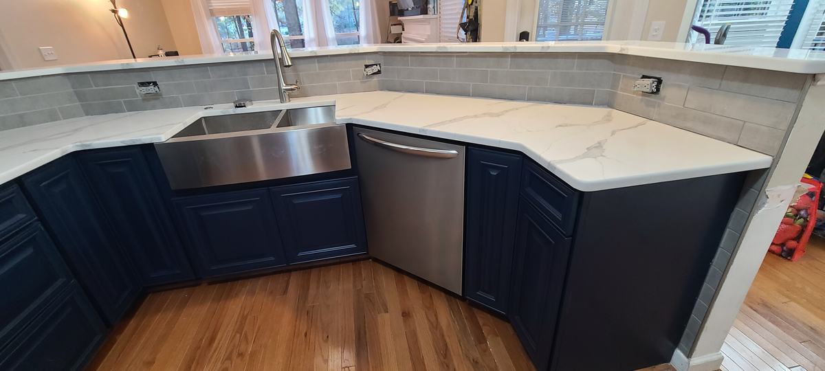 Kitchen after: navy lower cabinets, white quartz counters, farmhouse sink and new tile backsplash