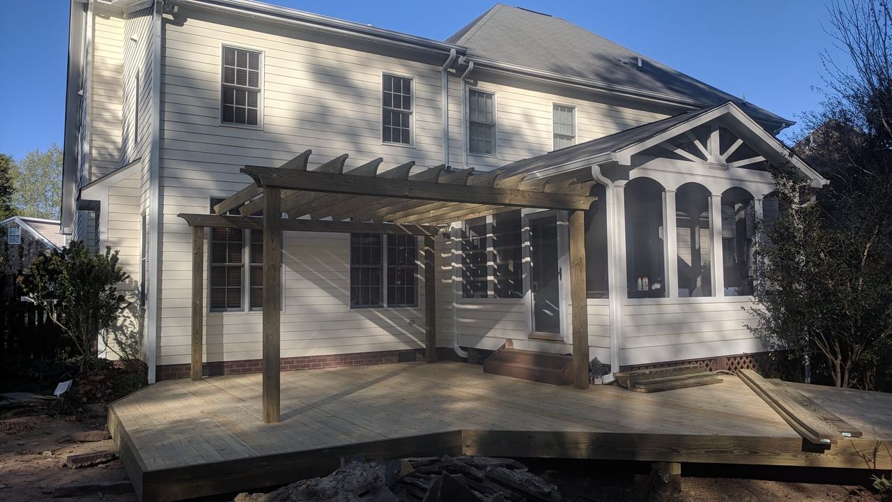 New deck with a pergola off the back of a white two-story house