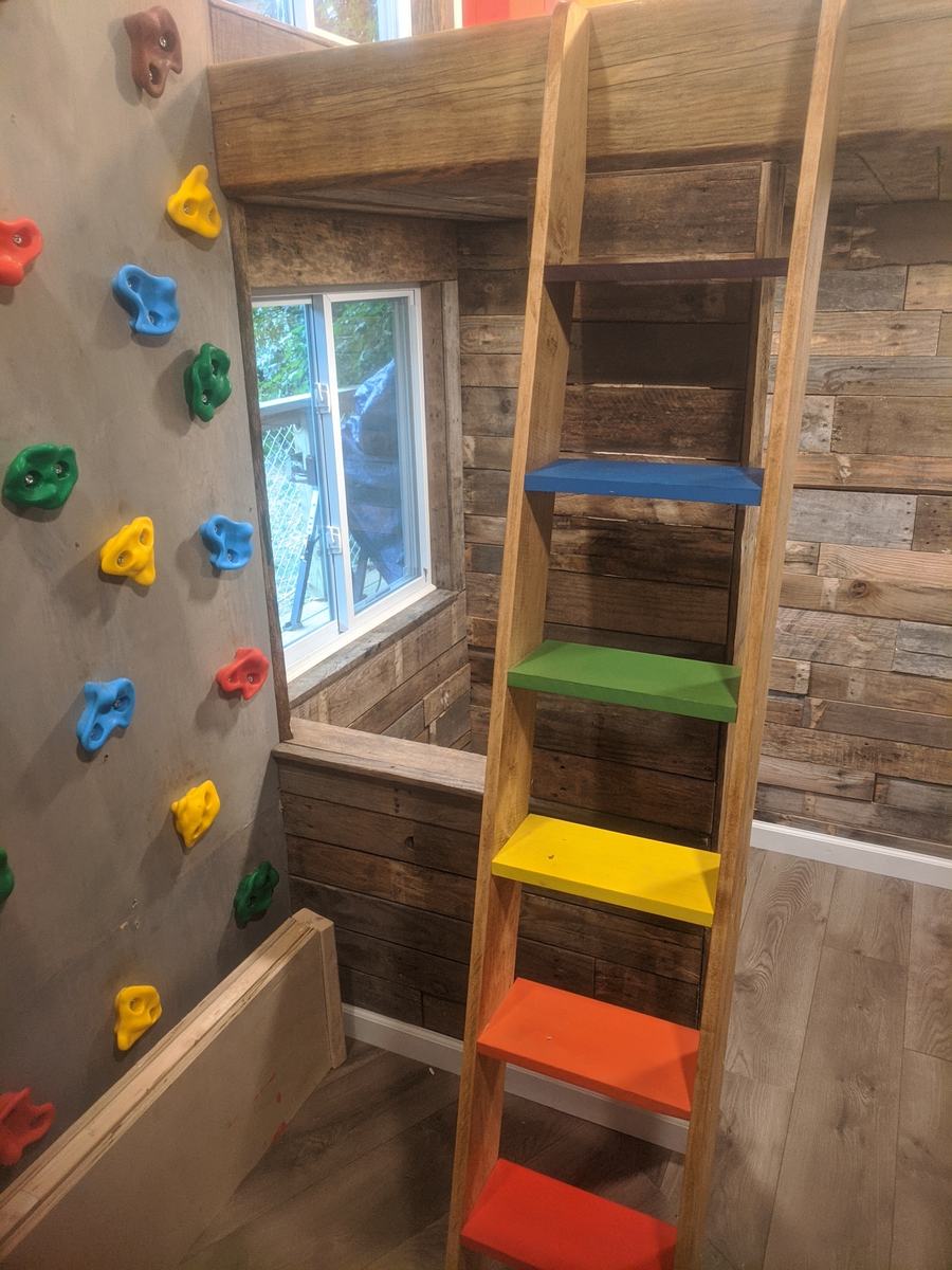 Kids’ playroom with a reclaimed-wood wall, climbing holds and a rainbow ladder